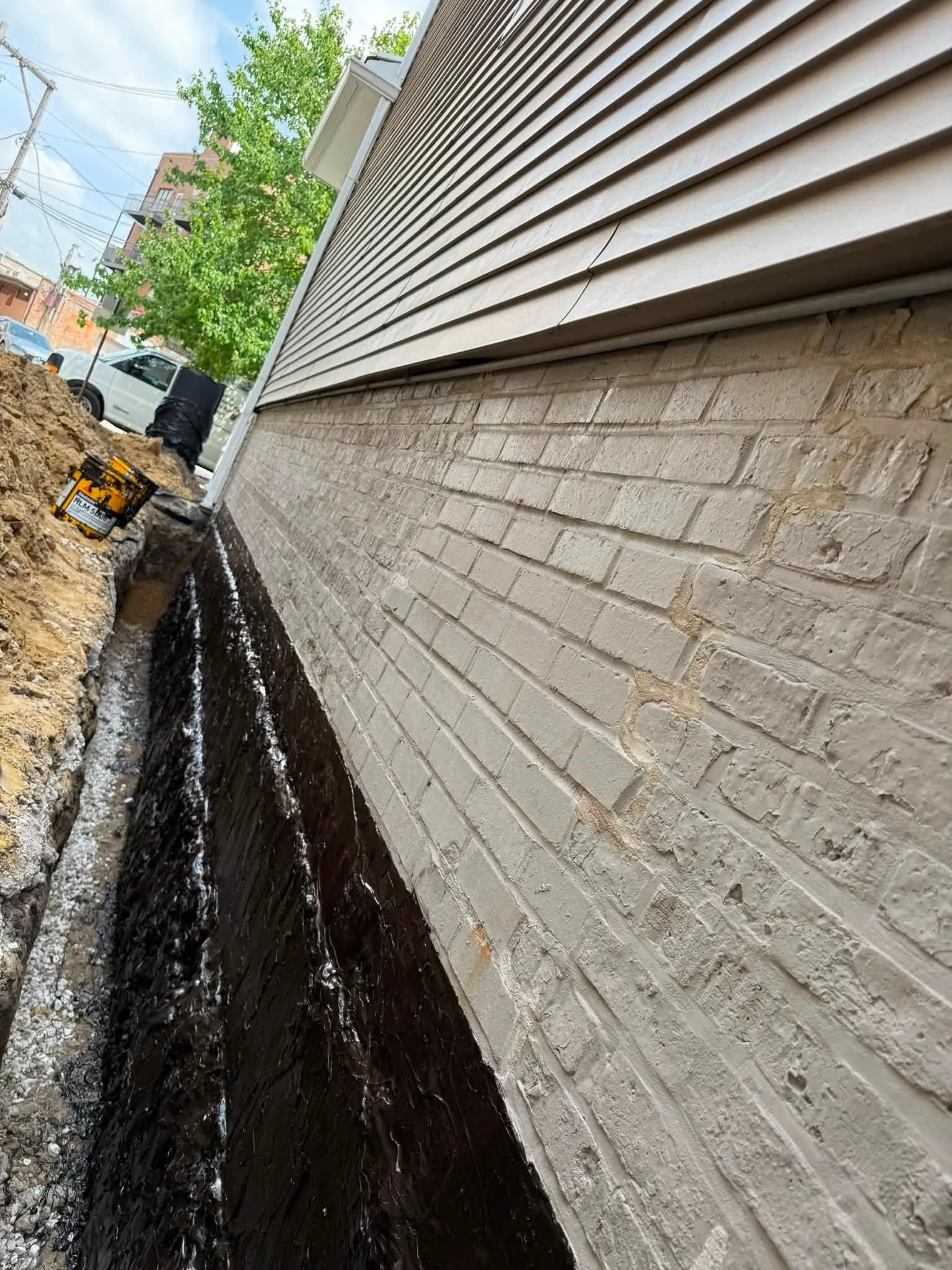Rubberised waterproofing membrane being applied to a painted brick foundation wall in an open trench, Etobicoke